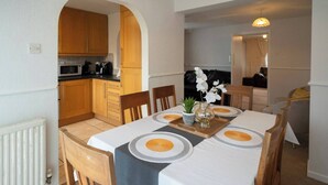 A dining area with a table set for four, wooden chairs, a white tablecloth, and a vase with flowers. - 3-bed Westhoughton, Contractors and Parking (Bolton)