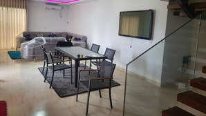 Un soggiorno moderno con un tavolo da pranzo in vetro, sedie, un divano e una TV a parete.