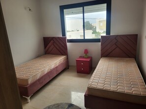 A bedroom with two beds, a nightstand, and a window. - A charming villa with swimming pool 400m (Hammamet)
