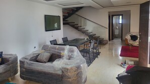 Un soggiorno moderno con un tavolo da pranzo in vetro, divani grigi, una scala e una TV montata a parete.