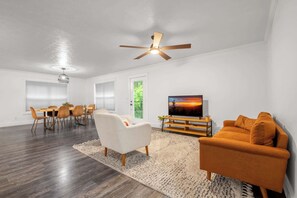 A modern living room with a dining area, a ceiling fan, a flat-screen TV, and a large window. - Smoky Pines Retreat, Sleeps 10, Hot Tub, Balcony (Sevierville)