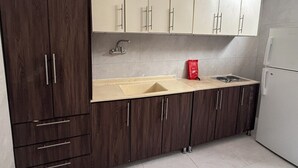 A kitchen with dark wooden cabinets, a beige countertop, a sink, a stove, and a white refrigerator. - Alsumo Suites (Ha'il)