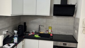 A compact kitchen with white cabinets, a black countertop, a built-in oven, and a ceiling light fixture. - Studio parking clim wifi parking downtown (Béziers)