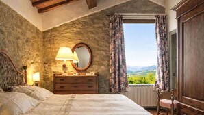 Ein Schlafzimmer mit Bett, Kommode, Lampe, Spiegel und einem Fenster mit Vorhängen.