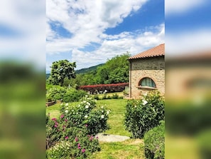 A stone building with a red-tiled roof, surrounded by a well-maintained garden with various plants and flowers. - Lovely apartment for 6 people with WIFI, A/C, pool, TV and panoramic view (Londa)