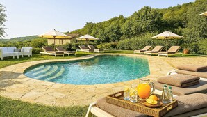Ein Pool mit Liegestühlen und Sonnenschirmen, umgeben von viel Grün.