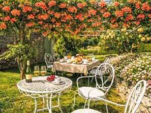 A garden patio with a table set for a meal, surrounded by lush greenery and flowering plants. - Lovely apartment for 6 people with WIFI, A/C, pool, TV and panoramic view (Londa)