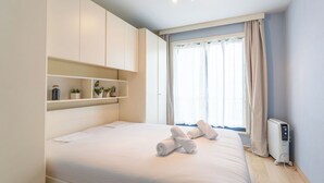 Een slaapkamer met een bed, inbouwkasten, een radiator en een raam met gordijnen.