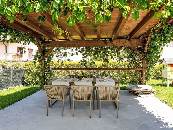 Un espace extérieur abrité, aménagé pour les repas, avec une pergola, des tables et des chaises.