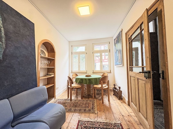 Una habitación acogedora con piso de madera, una mesa y sillas verdes, una estantería y un cuadro grande en la pared.
