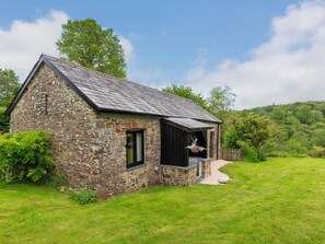 Ein Steinhaus mit geneigtem Dach, einer kleinen Veranda und einem Rasen.
