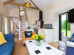 Ein modernes Wohnzimmer mit einer Couch, einem Couchtisch mit Blumenvase, einer Treppe, einer Küchenzeile und einem großen Fenster.