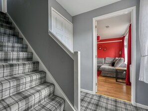 Eine Treppe mit Schachbrettmuster, eine graue Wand und ein rotes Zimmer mit einer Couch und Vorhängen.