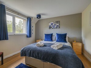Ein Schlafzimmer mit einem Bett, einem Nachttisch, einer Lampe und einem Fenster mit Vorhängen.