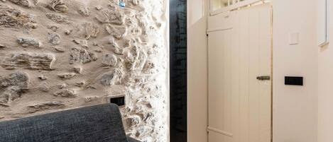 A room with a stone wall, a grey sofa, a white door, and a small window.