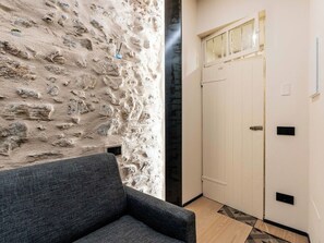 Ein Zimmer mit einer Steinwand, einem grauen Sofa, einer weißen Tür und einem kleinen Fenster.