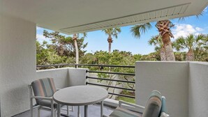 A balcony with a table and chairs, a view of palm trees, and a white wall. - The Flip Flop - 1BR w/ beach & lake access (Ponte Vedra Beach)