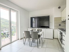 Eine moderne Küche mit großem Fernseher, Esstisch, Stühlen und Blick ins Freie.