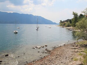 Ein ruhiger See mit Booten, einer felsigen Uferlinie und Bergen im Hintergrund.