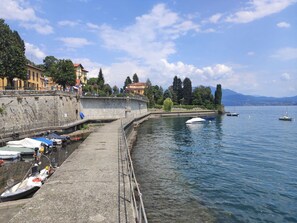 Eine Uferpromenade mit vertäuten Booten, einer Steinmauer und Gebäuden entlang des Ufers.