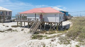 Un edificio frente a la playa con techo rojo, terraza de madera y una escalera que lleva a la entrada.