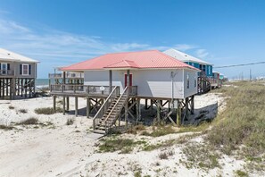 Ein Gebäude direkt am Strand mit rotem Dach, einer Holzterrasse und einer Treppe zum Eingang.