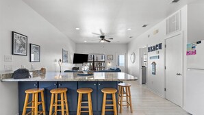 Una cocina moderna con una isla central, taburetes de bar, un ventilador de techo y un televisor.