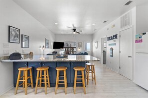Eine moderne Küche mit einer zentralen Kochinsel, Barhocker, Deckenventilator und Fernseher.