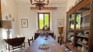 Un comedor con una larga mesa de madera, sillas, una araña y un aparador con puertas de vidrio.