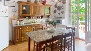 Una cocina con armarios de madera, encimera de granito, mesa de comedor con sillas y vista a la vegetación por la ventana.