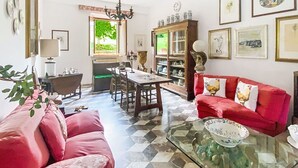 Un comedor con mesa, sillas, una lámpara de araña y un sofá rojo con cojines decorativos.