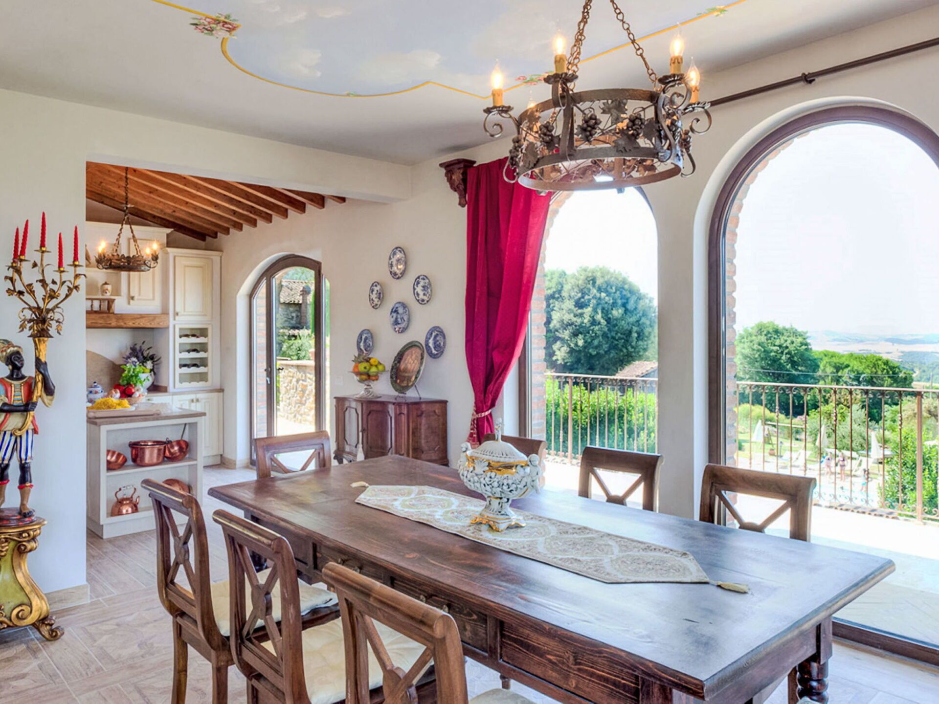 Un comedor con una mesa de madera, sillas y una araña. Se ve un jardín a través de amplias ventanas.