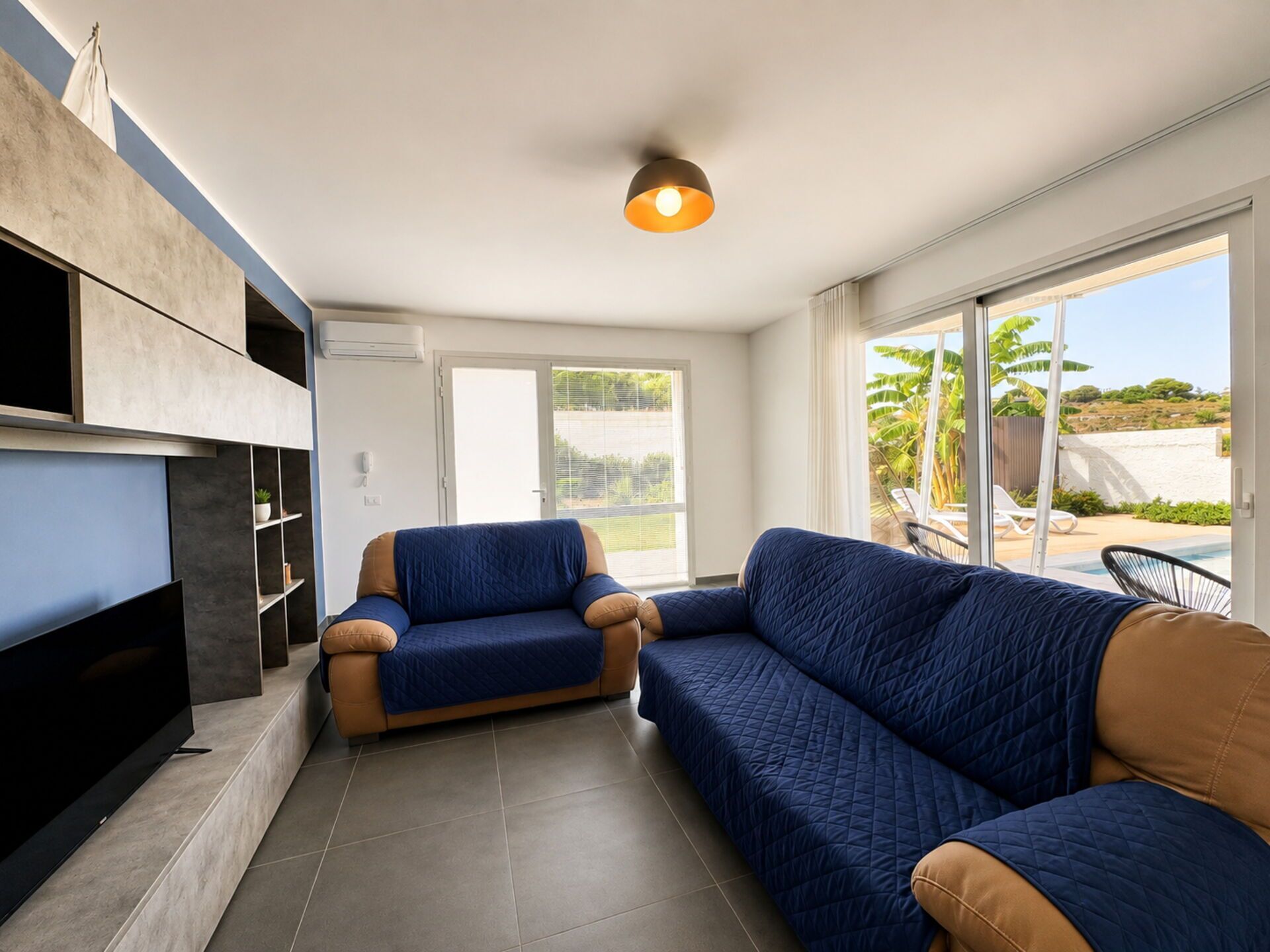 A modern living room with a flat-screen TV, two sofas, and a ceiling light.