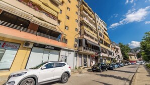 Ein mehrgeschossiges Gebäude mit Balkonen, Geschäften, darunter ein Schuhgeschäft, und parkenden Autos auf der Straße.