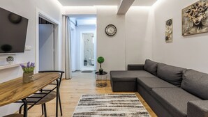 Ein modernes Wohnzimmer mit einem grauen Sofa, einem Holzesstisch und einem an der Wand befestigten Fernseher.