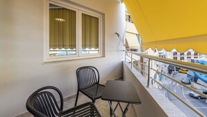 Ein Balkon mit zwei Stühlen und einem Tisch, ein Fenster mit Vorhängen und ein gelbes Markisen