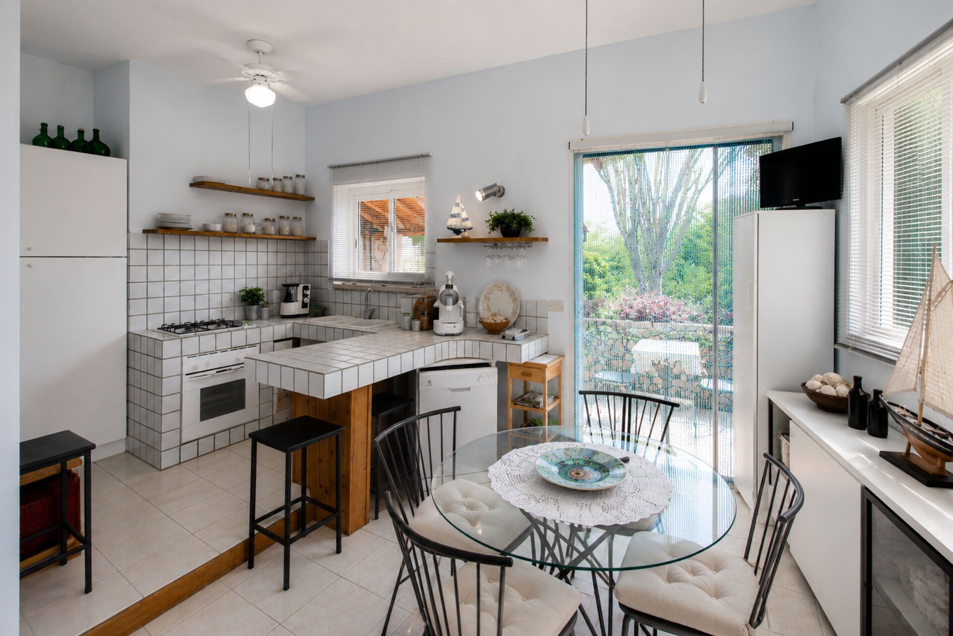 A modern kitchen with a central island, a dining area with a glass table, and a view of the outdoors.