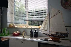Eine Küchenarbeitsplatte mit einem Modellsegelschiff, einem Fenster mit Jalousien und verschiedenen Küchenutensilien.