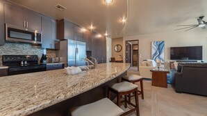 A modern kitchen with granite countertops, stainless steel appliances, and a built-in oven. There is a dining area with a bar stool and a sofa. - Las Palomas Phase II Coronado 801 Exceptional oceanfront 2BR 2BA Unit (Puerto Peñasco)