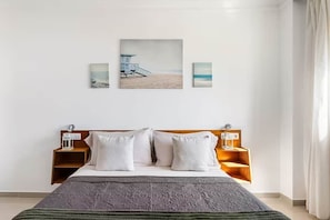 Ein Hotelzimmer mit Bett, Nachttisch, Holz-Kopfteil und einem Wandbild mit Strandmotiv.