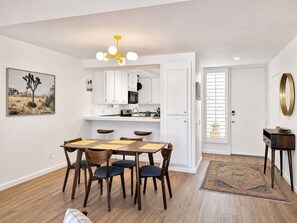 A modern kitchen with white cabinets, a dining area with a wooden table and chairs, and a small side table with a mirror. - Beautiful single level condo in south Palm Springs (Palm Springs)