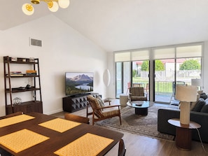 A modern living room with a dining table, sofa, TV, and a view of a backyard. - Beautiful single level condo in south Palm Springs (Palm Springs)