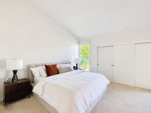 A bedroom with a bed, bedside tables, a wardrobe, and a window with a view of greenery. - Beautiful single level condo in south Palm Springs (Palm Springs)