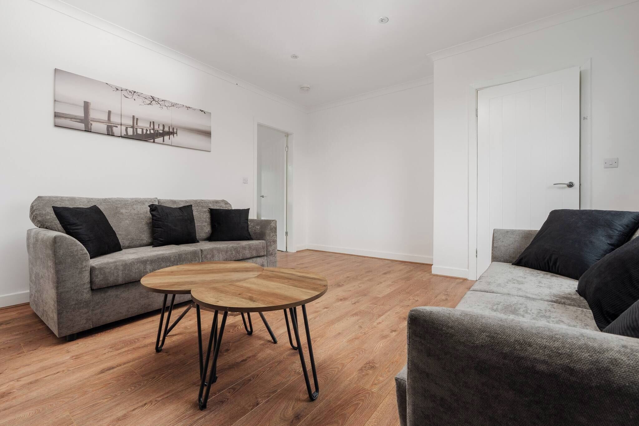 A modern living room with a grey sofa, a round wooden coffee table, and a painting on the wall.