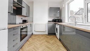 Una cocina moderna con armarios grises, encimera de madera, horno empotrado, lavadora y ventana con vistas.