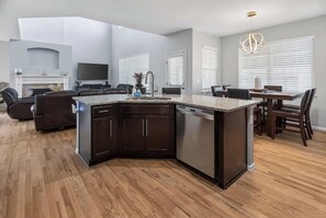 A modern kitchen with dark cabinetry, a granite countertop, and a built-in dishwasher. - 3BR Spacious Home with BBQ Patio,Backyard,Sleeps 6 (Aurora)