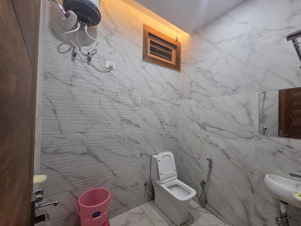 A bathroom with a toilet, shower, and sink, all against marble walls.