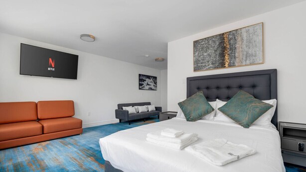 Une chambre d’hôtel avec un grand lit, un canapé, une télévision et des œuvres d’art accrochées aux murs.