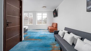 Une chambre d’hôtel moderne avec une grande fenêtre, un canapé, un fauteuil et une moquette bleue.