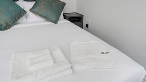 Un lit bien fait, avec des draps blancs, deux coussins turquoise et une serviette blanche pliée posée sur le côté.